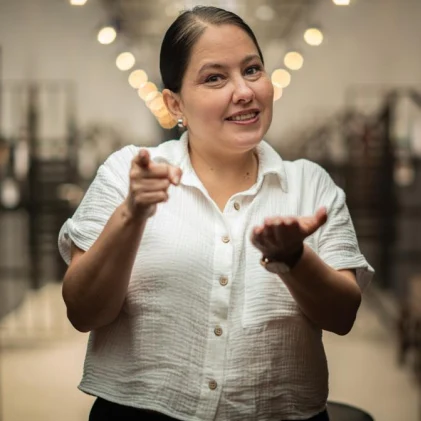 Mujer vestida con una blusa blanca, comunicándose por medio de lenguaje de señas